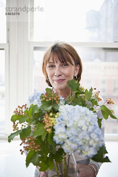 Eine reife Frau hält ein Blumenarrangement mit Hortensien.