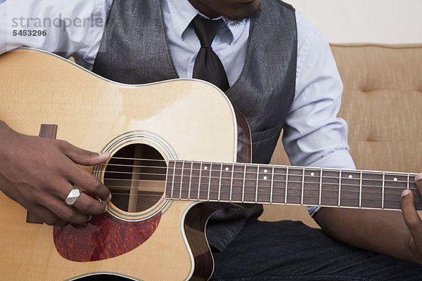 Ein junger Mann  der eine Akustikgitarre spielt  konzentriert sich auf den Mittelteil.