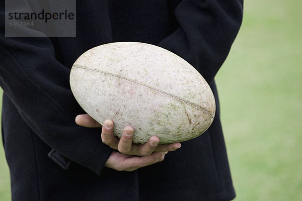 Ein Mann  der einen Rugbyball hinter seinem Rücken hält  Nahaufnahme der Hände.