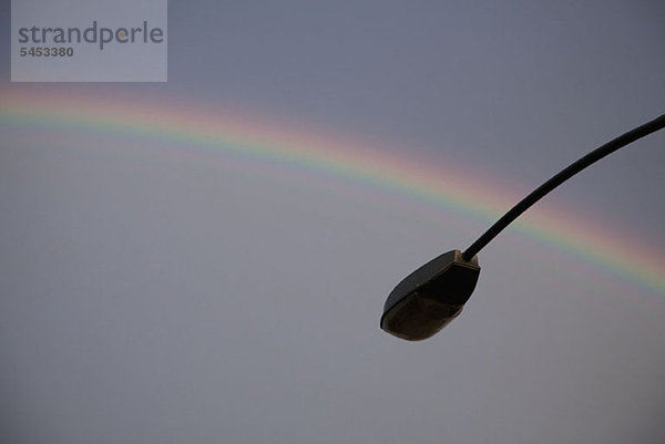 Ein Regenbogen im Rücken einer silhouettierten Straßenlampe