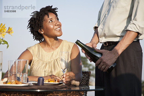 Ein Mann gießt Champagner für eine Frau auf einer Dachterrasse.