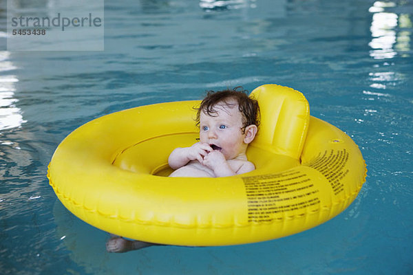 Ein kleines Mädchen  das in einem aufblasbaren Ring in einem Hallenbad schwimmt.