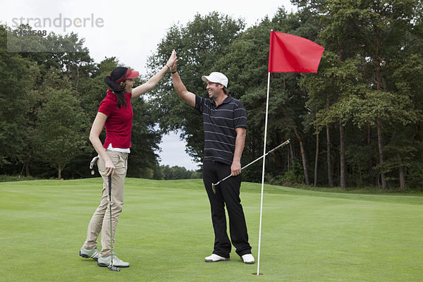 Ein weiblicher Golfer  der einen männlichen Golfer auf dem Putting Green hochhält.
