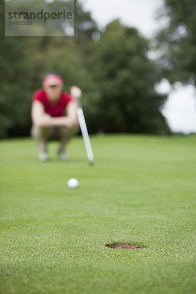 Ein Golfer  der den Abstand zum Loch studiert und sich auf das Loch konzentriert.