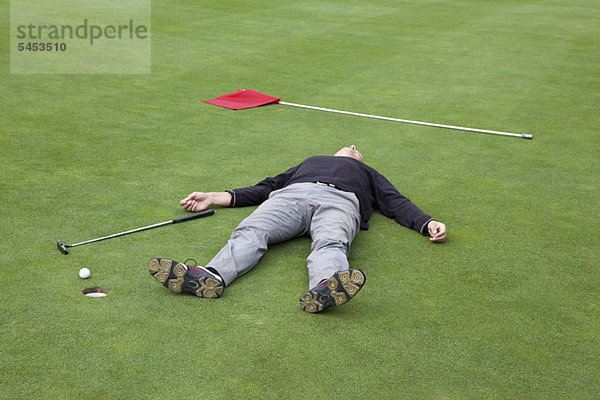 Ein verzweifelter Golfer  der auf dem Putting Green mit Ball am Lochrand liegt