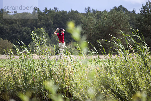 Eine Golfspielerin beim Abschlag  Fokus auf den Hintergrund