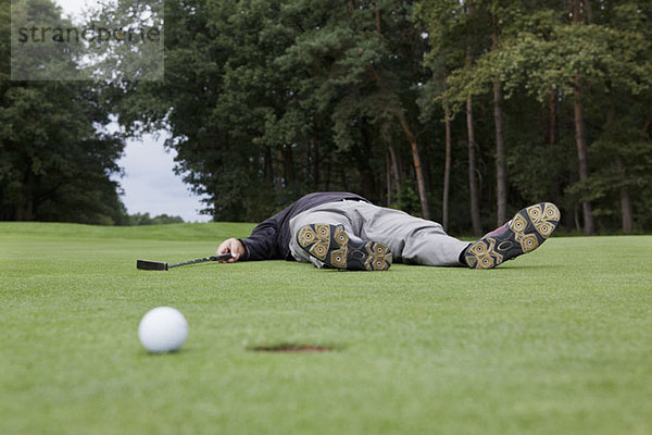 Ein verzweifelter Golfer  der auf dem Putting Green mit Ball am Lochrand liegt