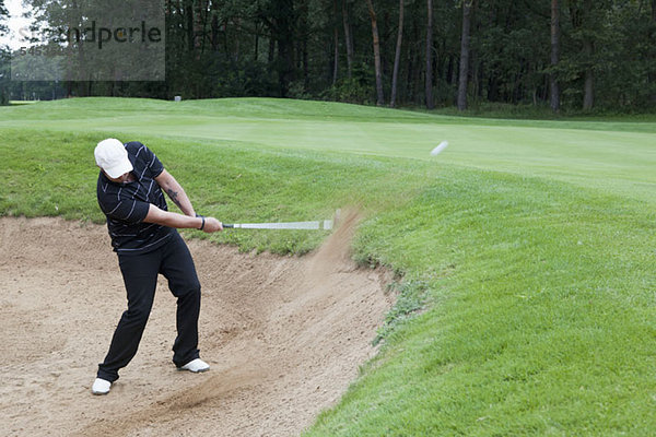 Ein Golfer  der einen Ball aus einer Sandfalle schlägt.