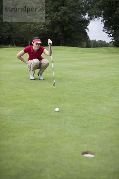 Eine Golferin  die sich hinhockt und die Entfernung zum Loch studiert.