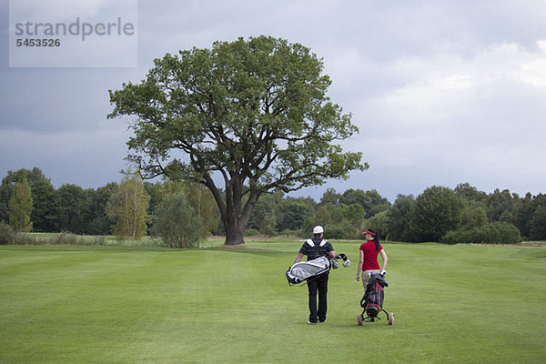 Eine Golferin und ein Golfer gehen mit ihren Golftaschen  Rückansicht