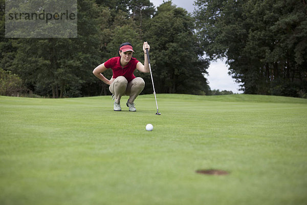 Eine Golferin  die sich hinhockt und die Entfernung zum Loch studiert.