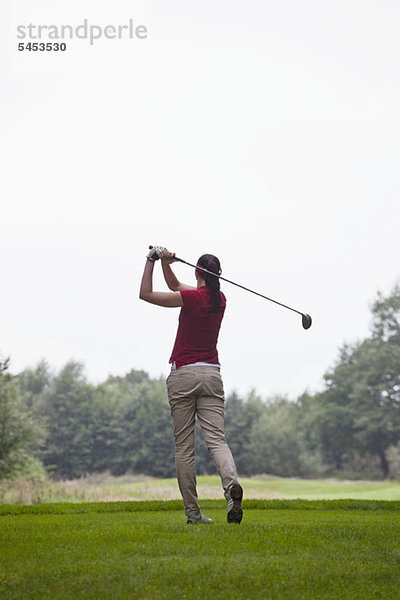 Eine Golfspielerin beim Abschlag  Rückansicht