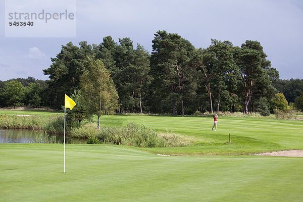 Putting Green mit Fahne  Golfer schwingt in der Ferne