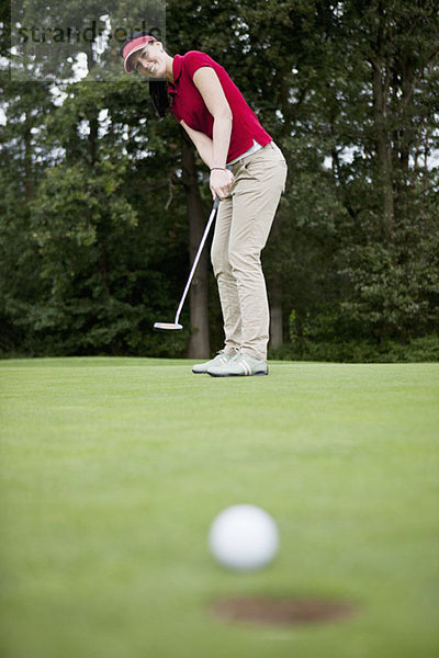 Eine Golferin beim Putten  Golfball am Lochrand