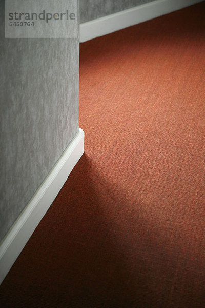 Kontraste von rotem Teppich gegen weiße Sockelleiste und graue Wand