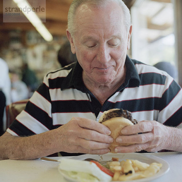 Ein älterer Mann macht sich bereit  einen Hamburger zu essen.