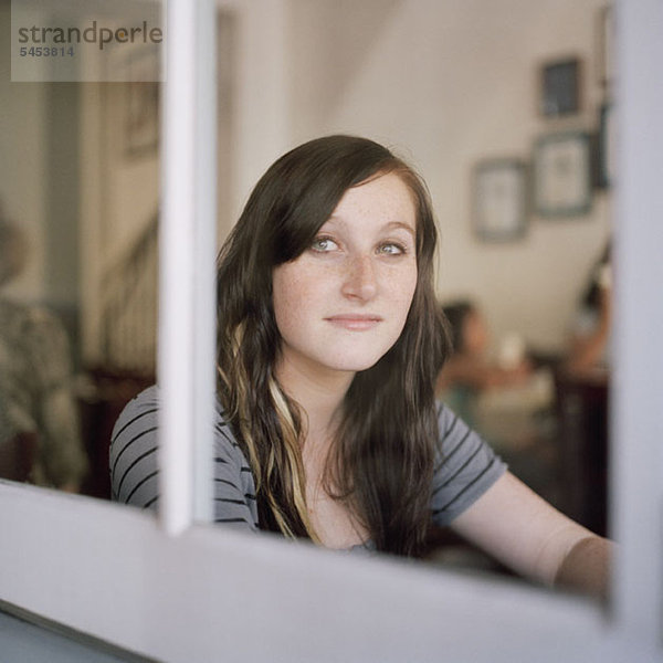 Eine junge Frau  die durch ein Fenster in Kontemplation schaut.