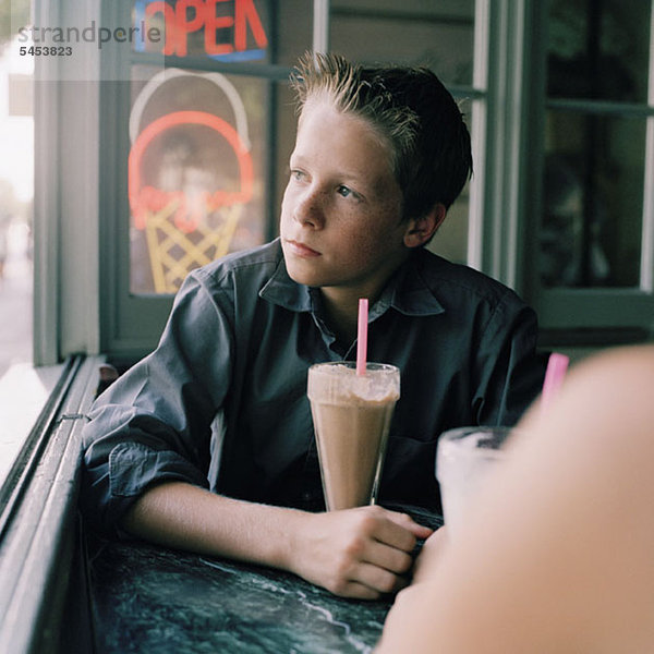 Ein ernsthafter Teenager mit einem Milchshake  der aus dem Fenster schaut.