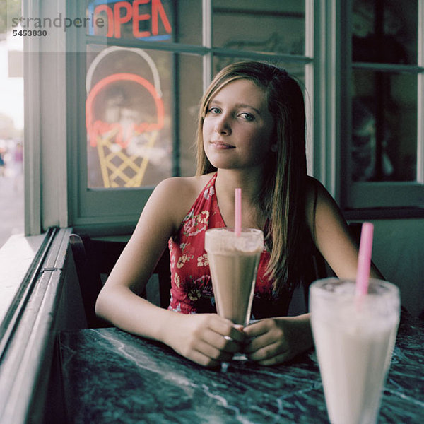 Ein junges Mädchen sitzt mit einem Milchshake am Tisch.