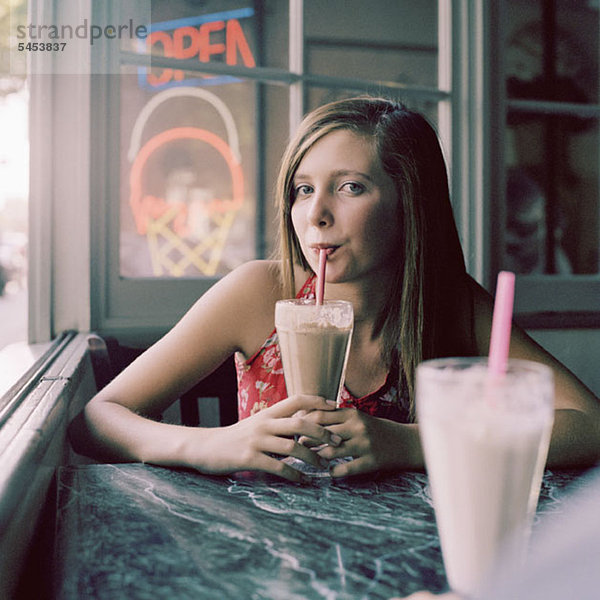 Ein Teenager-Mädchen trinkt einen Milchshake in einem Diner.