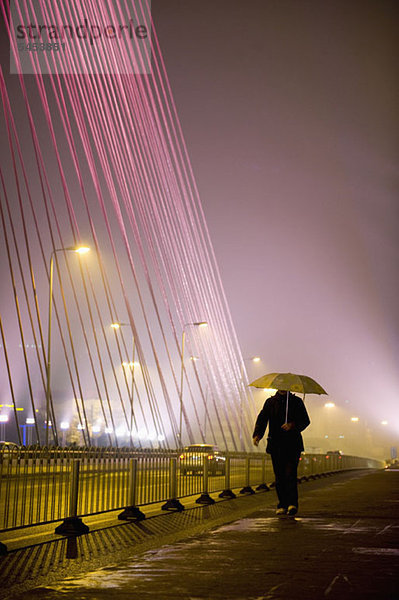 Ein Mann  der eine Stadtstraße entlanggeht und einen Regenschirm hält.