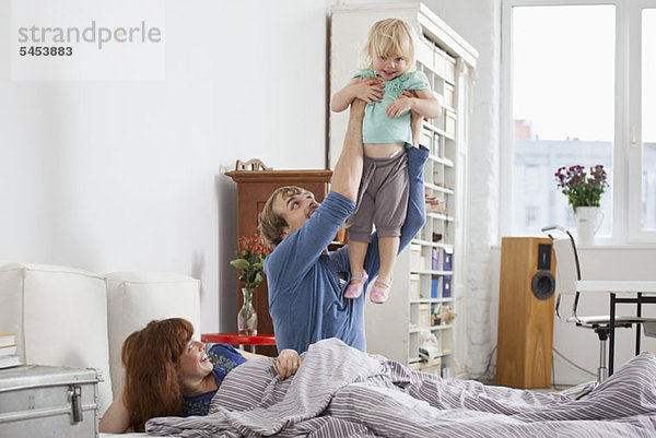 Ein Paar im Bett  ein Mann  der seine Tochter in der Luft hält.