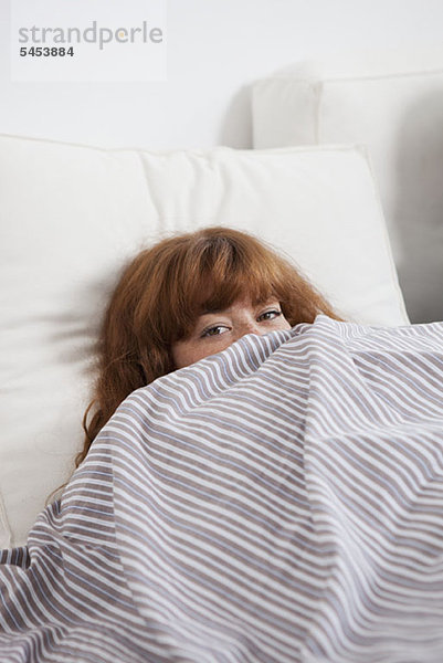 Eine Frau  die von hinten auf eine Bettdecke im Bett schaut.