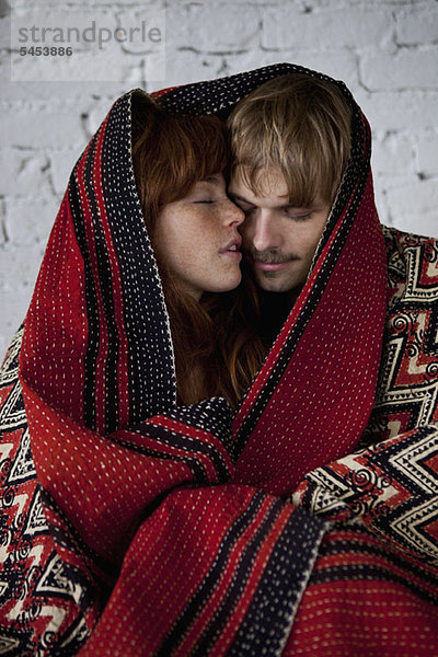 Ein sinnliches junges Paar in eine Decke gehüllt.