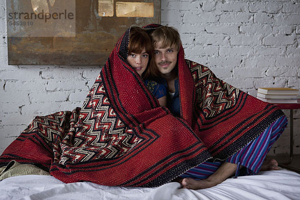 Ein ruhiges Paar  eingehüllt in eine Decke  die auf einem Bett sitzt.