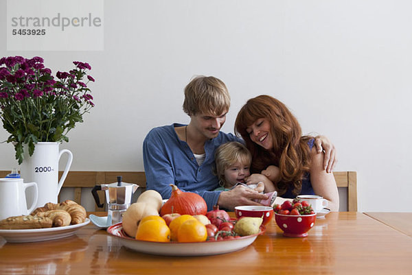 Eine junge Familie sitzt Seite an Seite beim Frühstück.