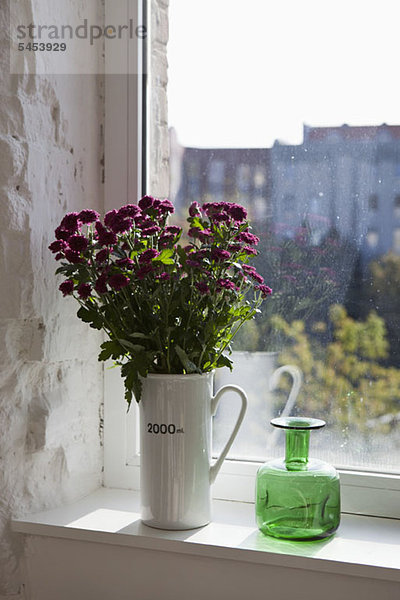 Grüne Flasche und Blumenstrauß auf der Fensterbank