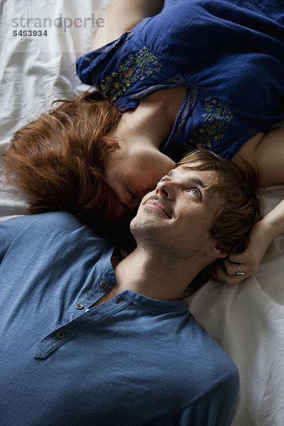 Ein junges Paar liegt Kopf an Kopf auf einem Bett.