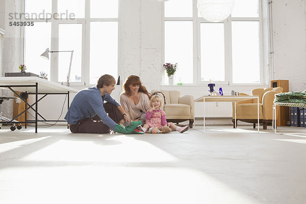 Eine junge  hippe Familie spielt zusammen auf dem Wohnzimmerboden.