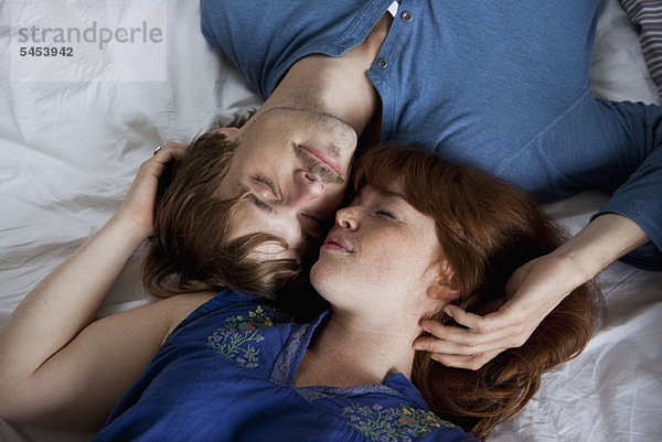 Ein junges Paar liegt Kopf an Kopf auf einem Bett  die Augen geschlossen.