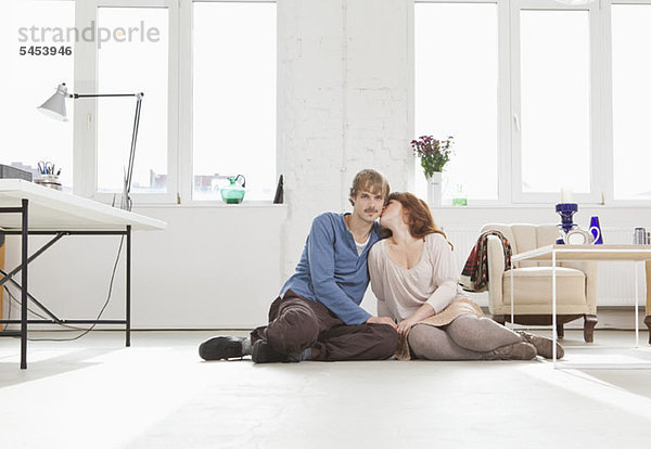 Ein junges  liebevolles Paar sitzt Seite an Seite auf dem Boden.