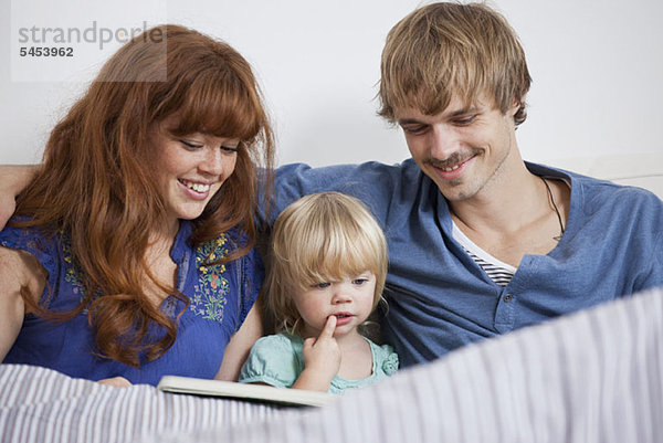 Eine junge Familie beim Lesen eines Bilderbuches im Bett