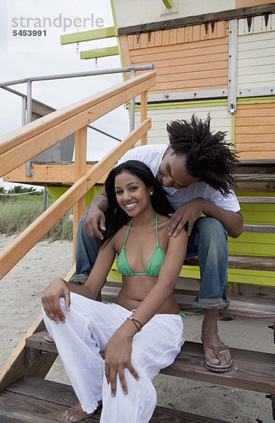 Ein junges glückliches Paar sitzt auf einer Treppe am Strand.