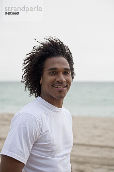 Ein cooler junger Mann steht an einem windigen Strand.
