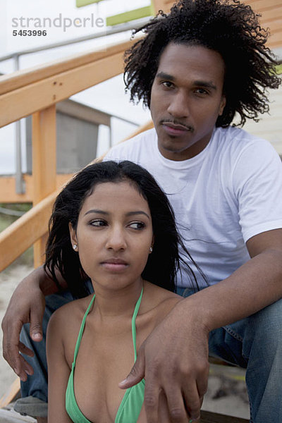 Ein junges seriöses Paar sitzt auf einer Treppe am Strand.