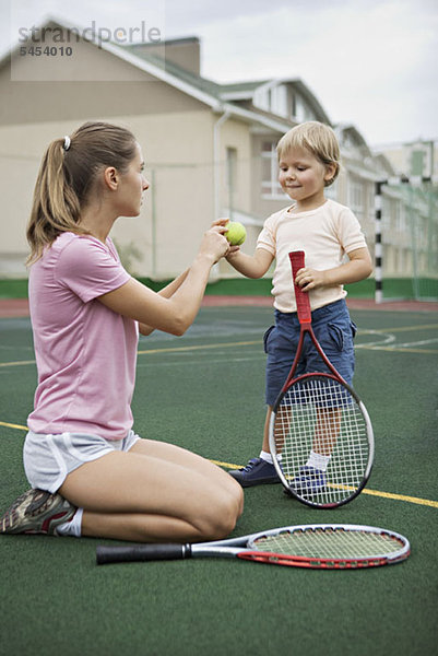 Eine Mutter  die ihrem kleinen Sohn Tennis beibringt.