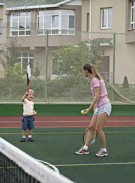 Eine Mutter bereitet sich darauf vor  ihrem kleinen Sohn einen Tennisball zu servieren.