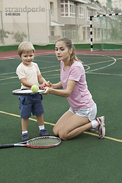 Eine Mutter  die ihrem Sohn beibringt  wie man einen Tennisball auf einem Schläger balanciert.