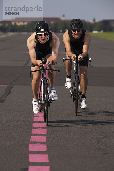 Zwei Radfahrer auf Rennrädern  die auf einer markierten Straße radeln.