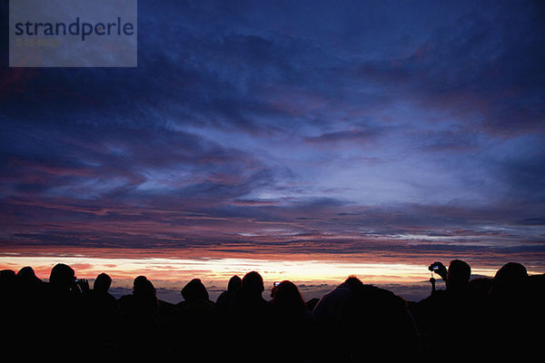 Reihe von Silhouetten  die den dramatischen Himmel betrachten