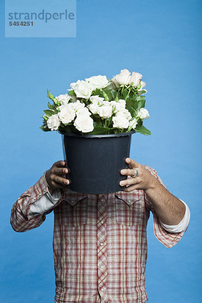 Ein Mann hält einen schwarzen Eimer Blumen vor sein Gesicht.