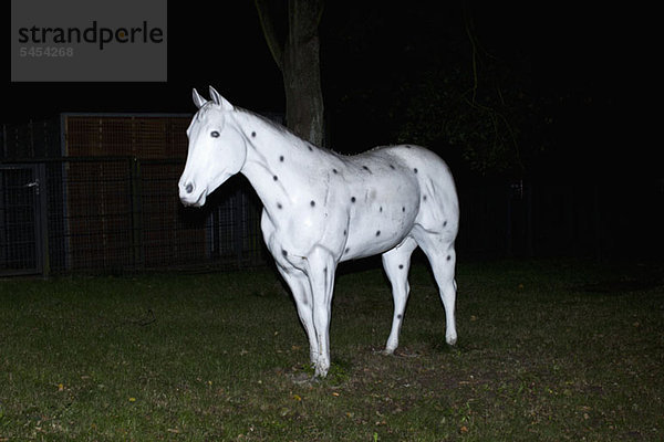 Künstliches weißes Pferd auf Gras mit schwarzen Punkten verziert