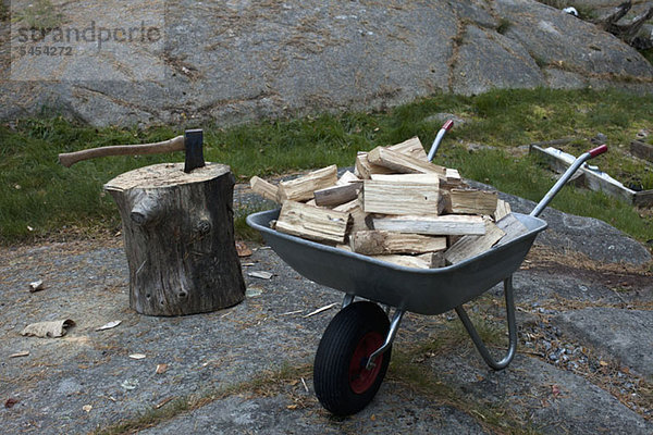 Baumstämme in Schubkarre und Axt im Baumstamm