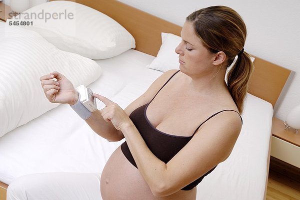 Nackte schwangere Frau beim Blutdruckmessen