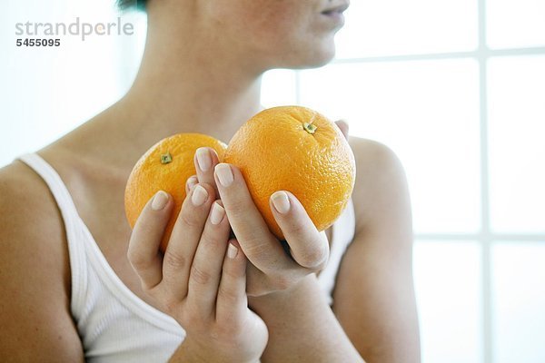 Weibliche Hände halten zwei Orangen.