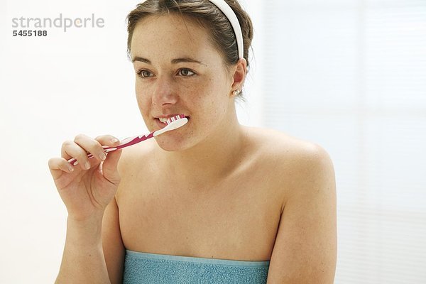 junge Frau bekleidet mit einem Handtuch putzt sich die Zähne mit Zahnbürste